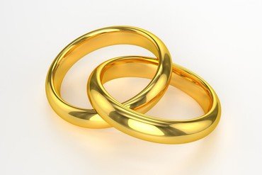 Zwei verschlungene, glänzende goldene Eheringe auf einer weißen Oberfläche.